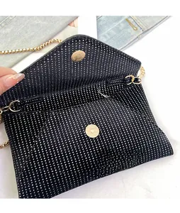Detail of the golden magnetic buckle and black rhinestone texture on the envelope bag