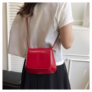 Detail of red glossy patent leather shell bag shown on model in a minimalist setting