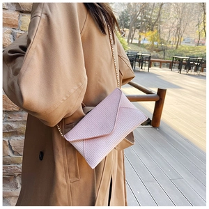 Pink woven envelope crossbody bag with a delicate gold chain shown on a wood terrace