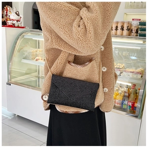 Detail of black rhinestone envelope bag with delicate gold chain strap for women