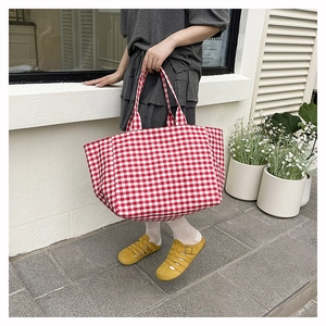 Woman carrying a red and white checkered canvas tote bag in an outdoor setting