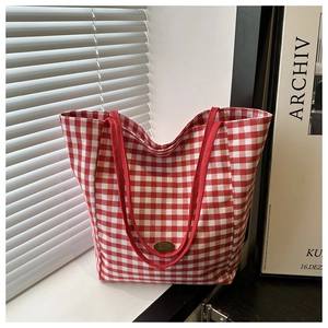Détail du sac cabas en toile à carreaux rouge et blanc avec étiquette métallique