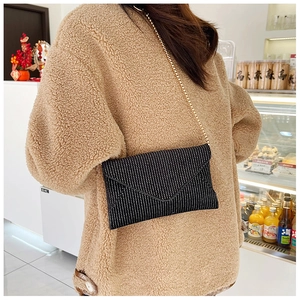 Black envelope crossbody bag with sparkling rhinestones and gold chain shown on a model