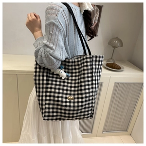 Detail of checkered tote bag with a cartoon doll pendant and metal brand logo plate