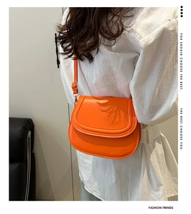 Detail of vibrant orange saddle bag in glossy PU leather with adjustable shoulder strap