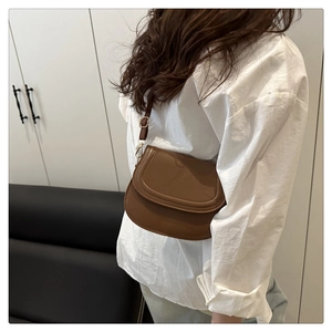 Brown faux leather saddle bag with gold hardware worn by model in a side-view pose