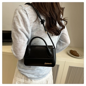 Détail du sac à bandoulière en cuir noir avec un logo élégant en métal doré sur le coin