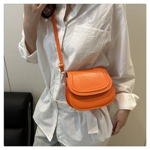 Detail of a vibrant orange leather saddle bag featuring a smooth matte finish and neat stitching