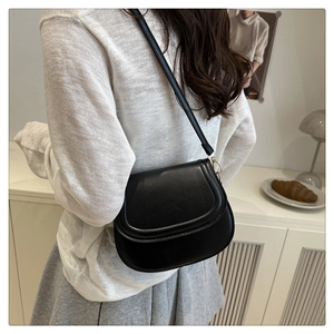 Classic black leather saddle bag with adjustable strap worn by a model in casual style