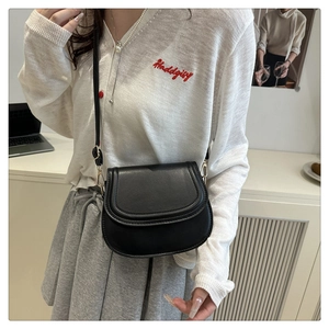Close-up of a black matte leather saddle bag styled with a white knit cardigan