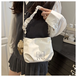 Detail of white satiny shoulder bag featuring ruffled straps and a cute bear pendant