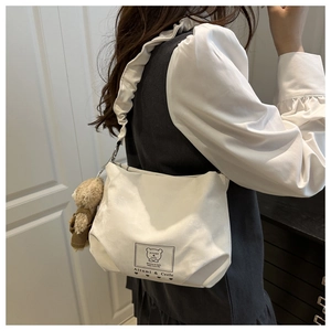 Detail of white ruffle strap handbag with teddy bear charm and brand logo patch