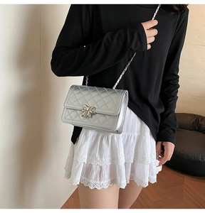 Détail d'un sac téléphone matelassé argenté avec nœud métallique et bandoulière chaîne