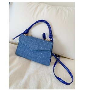 Detail of blue denim crossbody bag with floral texture and royal blue leather handle