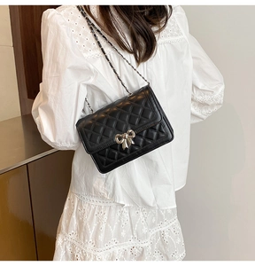 Détail d'un sac matelassé noir avec fermoir papillon doré porté à l'épaule pour femme
