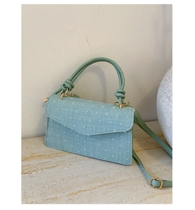 Close-up of mint green textured fabric handbag with gold hardware and knotted handle