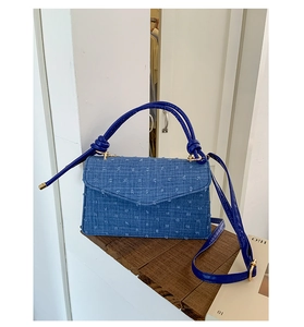 Close-up of blue denim small square bag with 3D pom-pom texture and knotted top handles