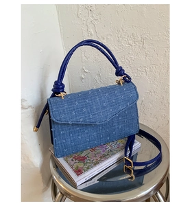 Blue denim textured flap handbag with square pattern detail on an artistic metal stool