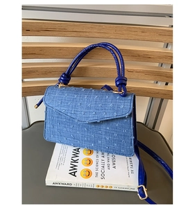 Detailed view of blue polka dot denim shoulder bag on a grey cushion with books