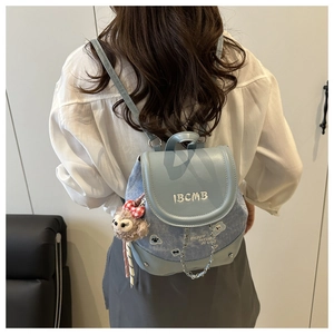 Detail of blue denim mini backpack featuring embroidered IBCMB text and StellaLou plush charm
