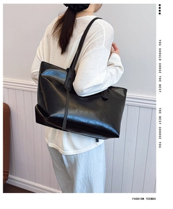 Side view of a large black glossy tote bag worn by a model for a chic commute style