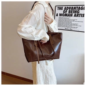 Large dark brown leather tote bag worn on shoulder by model in a white minimalist shirt