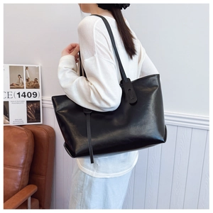 Close-up of a black glossy PU tote bag showing spacious design and slim shoulder straps