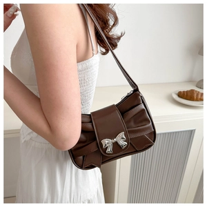 Detail of silver bow buckle and pleated leather texture on dark brown underarm bag