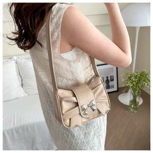 Détail du sac beige avec grand nœud et boucle en métal argenté porté par le modèle
