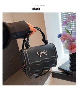 Détail du sac bandoulière noir avec rabat ondulé et décoration nœud doré