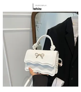 Détail d'un sac bandoulière blanc en cuir PU avec nœud doré et rabat ondulé
