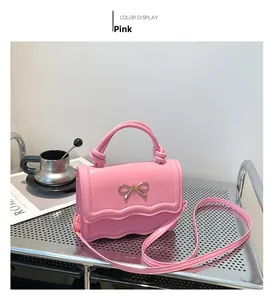 Détail du sac bandoulière rose avec boucle nœud doré et design bord ondulé