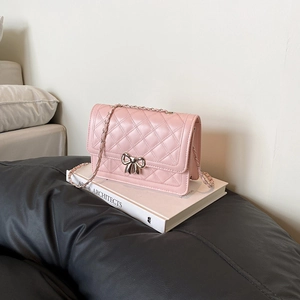 Sac bandoulière rose matelassé avec boucle nœud en métal sur un fond de livre épuré