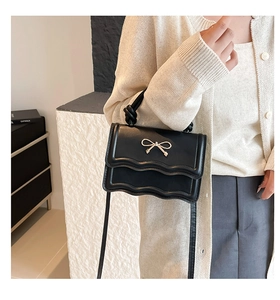 Detail of black leather handbag with wavy edge and golden bow clasp on a model