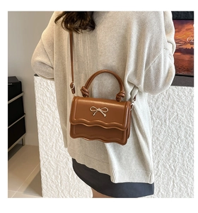 Detail of caramel brown crossbody bag with scalloped flap and silver bow clasp