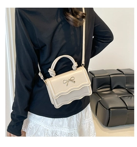 Close-up of cream crossbody bag with golden bow and scalloped edge detail worn by model