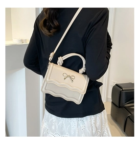Detailed back view of a creamy white handbag with wave edge and gold bow accent