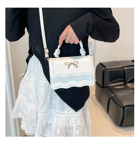 Detail of white PU leather crossbody bag with wavy edge and metal bow accessory