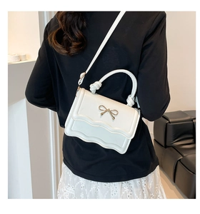 Close-up of white wave-edge crossbody bag with a gold bow buckle worn by a model