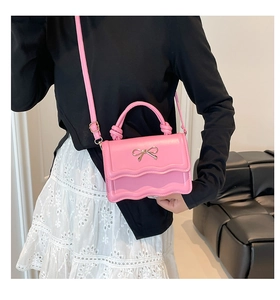 Detail of pink crossbody bag with scalloped flap and golden bow buckle worn by model