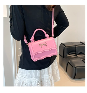 Close-up of pink crossbody bag with golden bow and scalloped edge detail worn by model