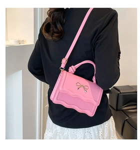 Close-up of pink crossbody bag featuring wave edge flap and gold bow ornament
