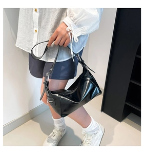 Detail of black glossy patent leather shoulder bag with silver hardware and adjustable strap