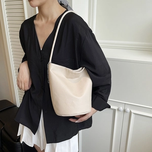 Off-white lychee grain leather bucket bag with silver chain strap worn by a model