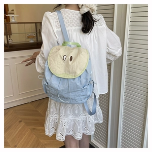 Blue and beige student backpack with cute cartoon eye design shown in a cozy cafe setting