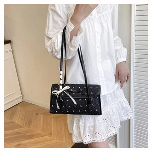Detail view of black quilted shoulder bag with white bow pendant and floral embroidery