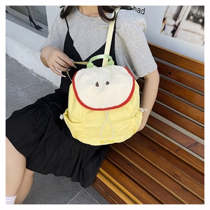 Detail of yellow apple-shaped backpack showing creative 3D fruit design and embroidered core
