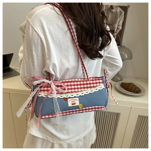 Close-up of blue denim underarm bag with red plaid bow and delicate lace trim detail