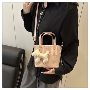 Bolso tipo cubo rosa con lazo, cuero granulado y colgante de perrito en una modelo