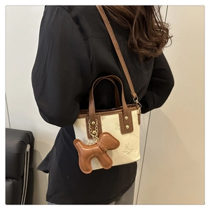 Detalle del bolso de cubo con relieve de mariposas y colgante de perrito marrón